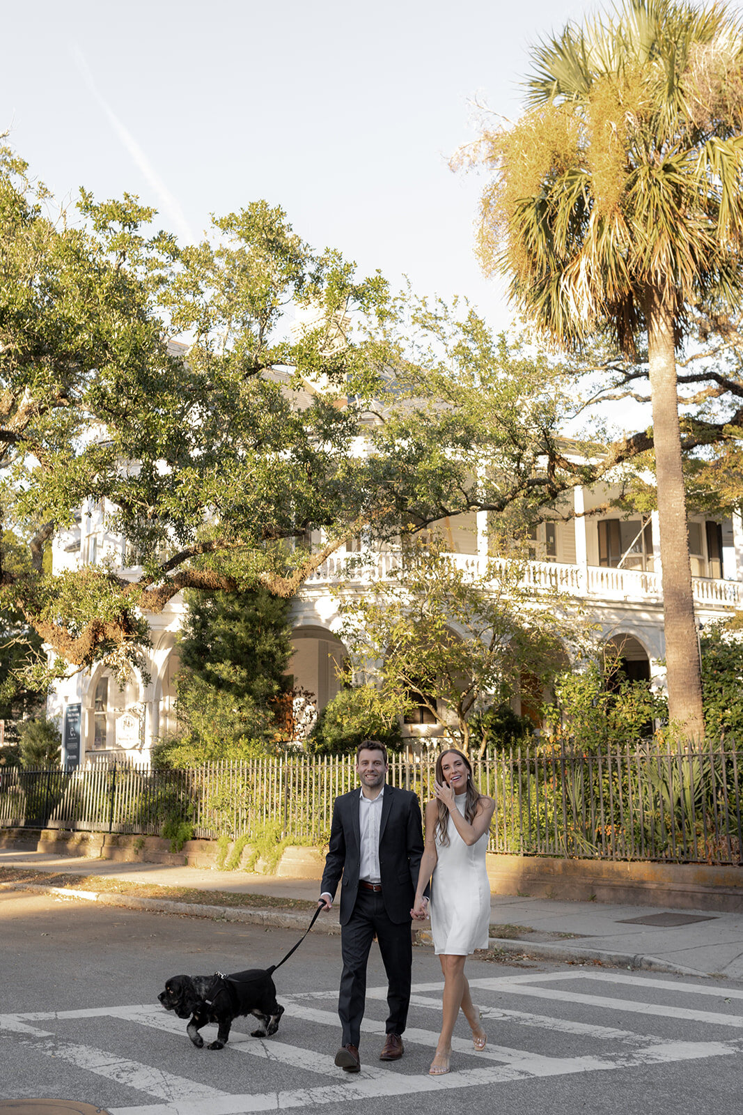 Couple with dog at photo session with Charleston houses and greenery in background