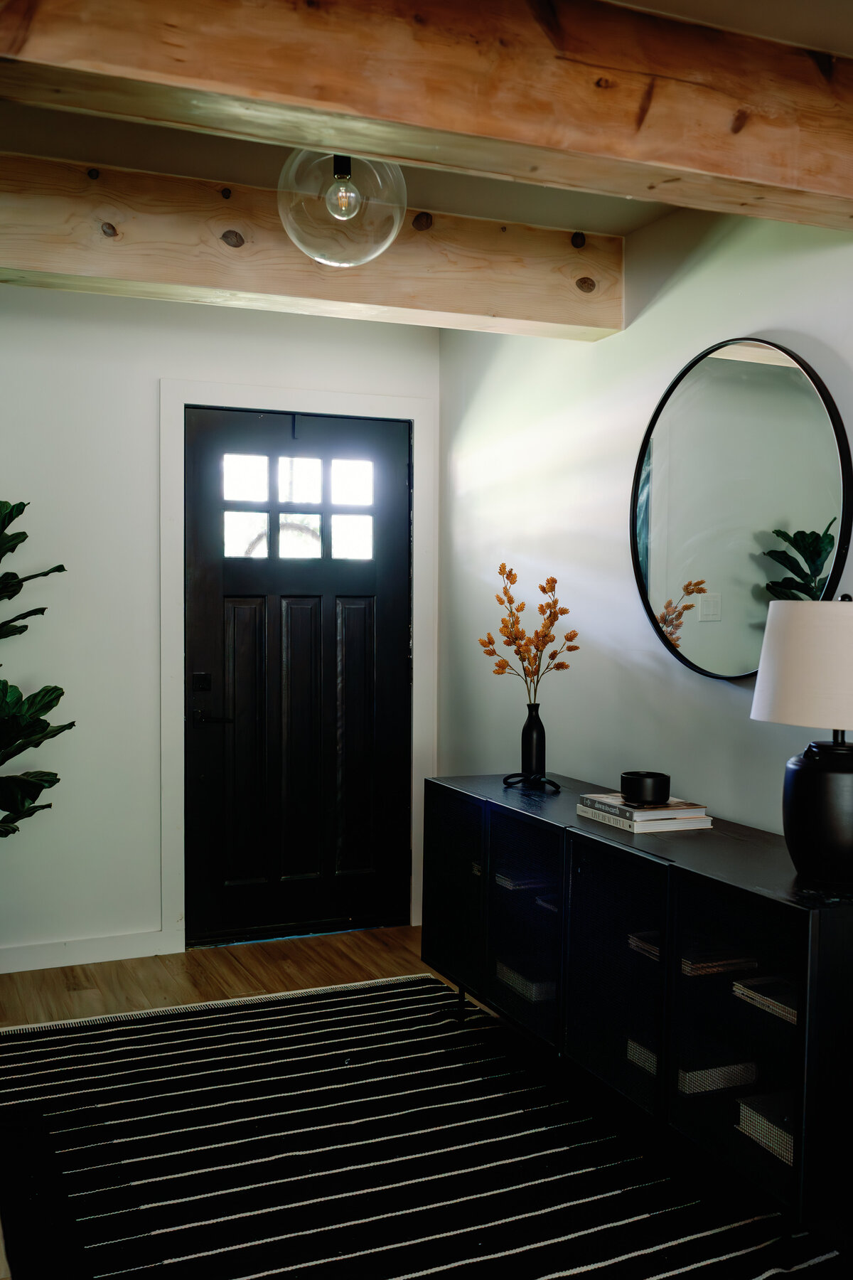 entry with black door, wood beams, glass light fixture, circle mirror and black buffet cabinet