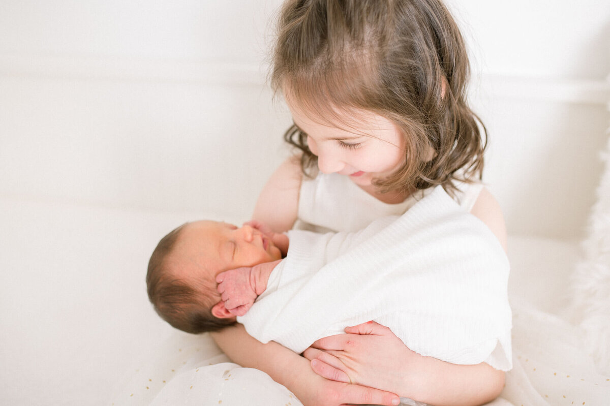 Big sister looking down at newborn sister with love. Captured by Niagara newborn photographer