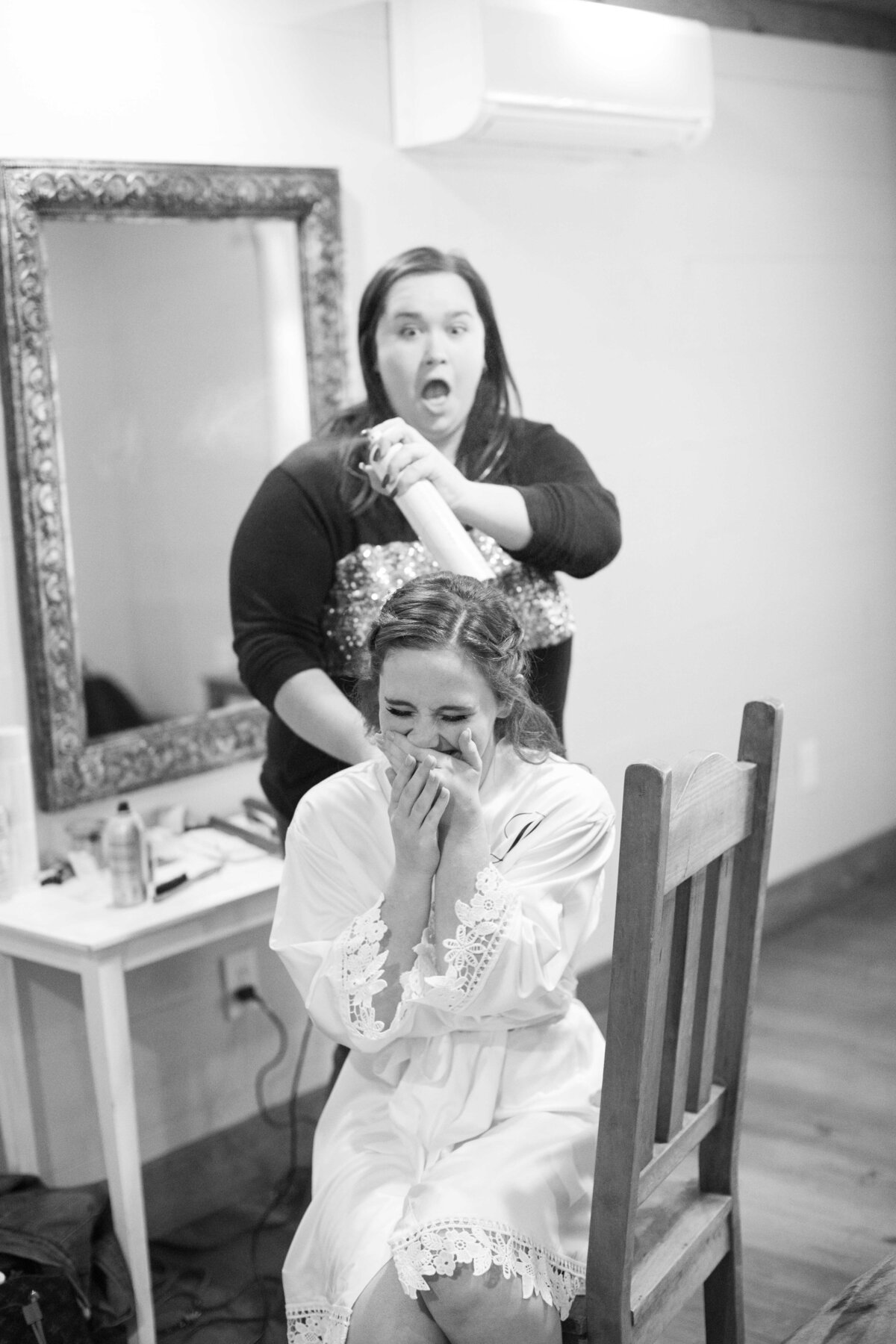 bride laughs as hair stylist sprays during preparations for wedding at Milltown Historic District in New Braunfels Texas