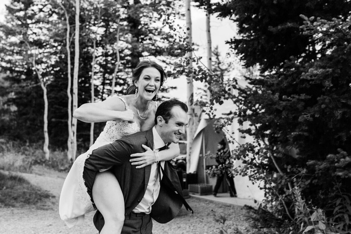 A groom gives his bride a piggyback ride after their elopement in an aspen grove