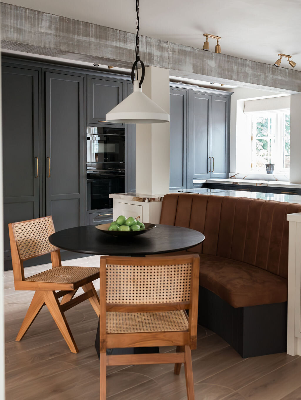 Modern kitchen with black cabinets, light wooden floor, and a built-in seating area with two wooden chairs and a small table