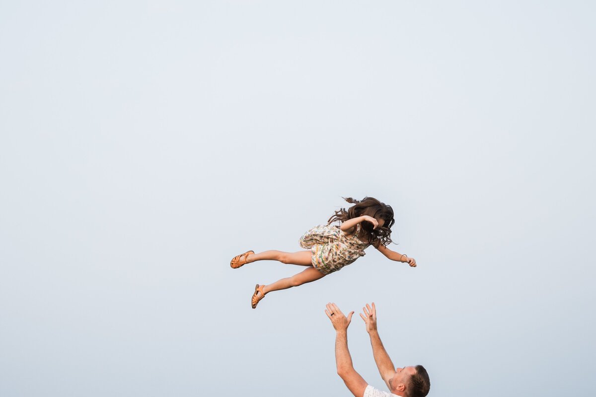 A child being playfully tossed into the air by an adult against a clear sky background, captured by a skilled Pittsburgh family photographer.