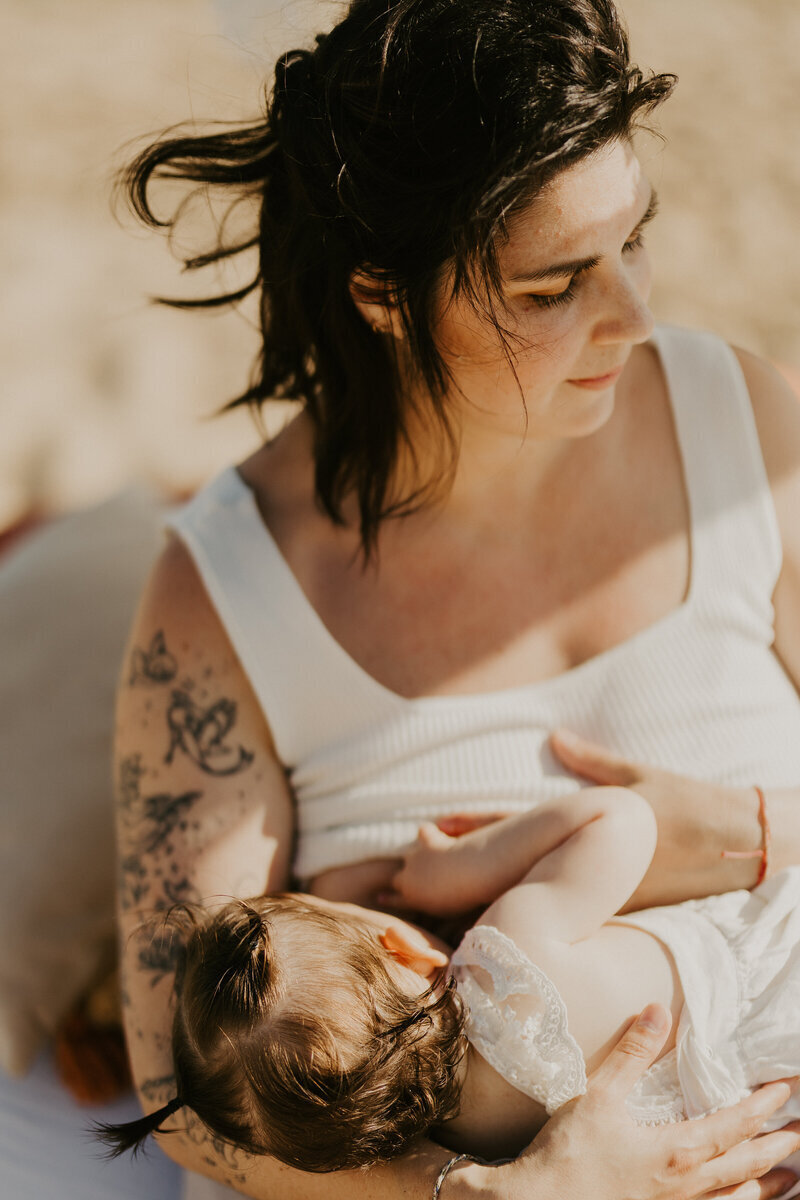 Maman donnant le sein à sa fille dans un décor cosy installé sur la plage. Photo prise par Laura Termeau photographie, lors d'une séance photo maternité.