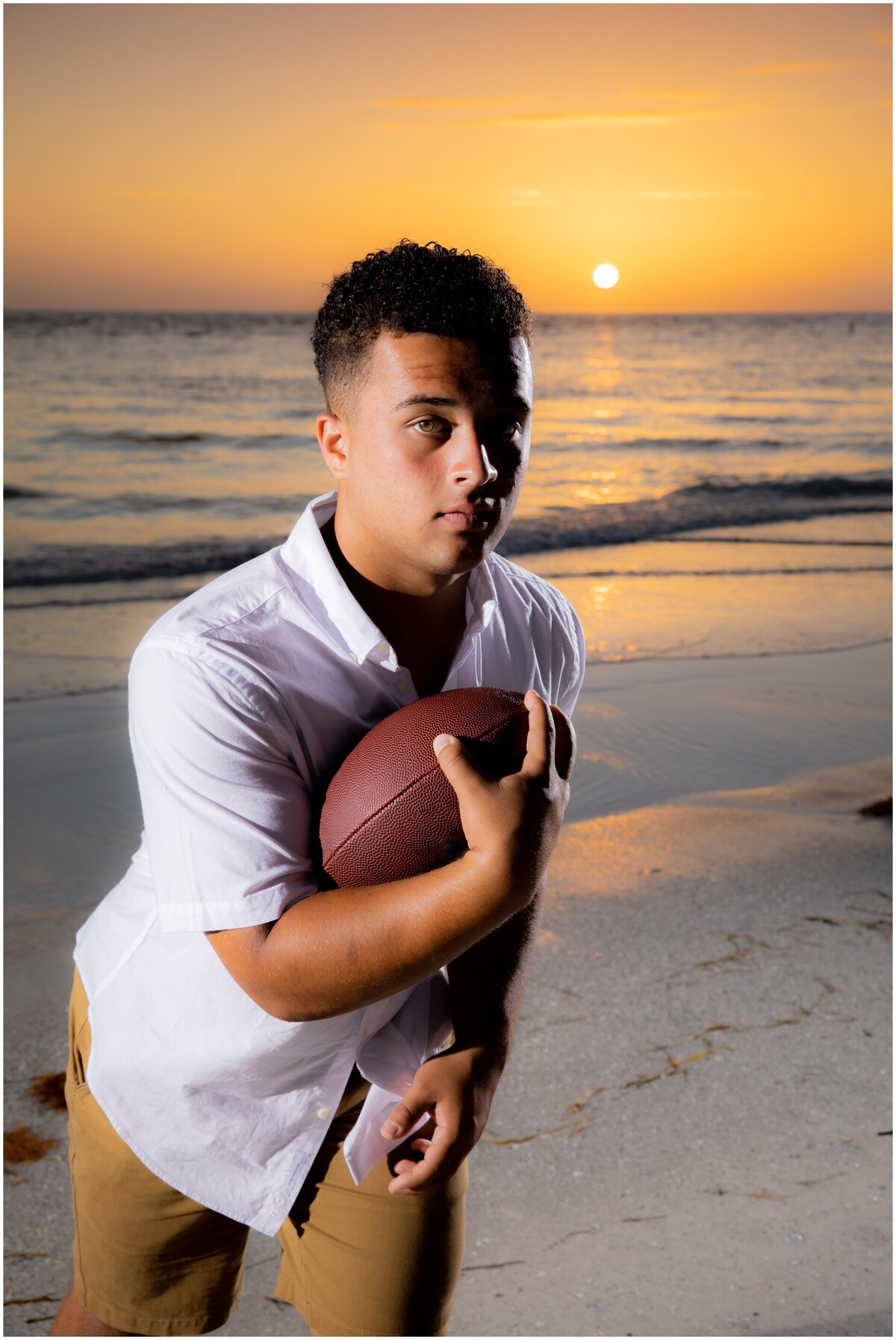 High school senior portrait of boy holding a  football captured by  love and style photography on Bradenton Beach