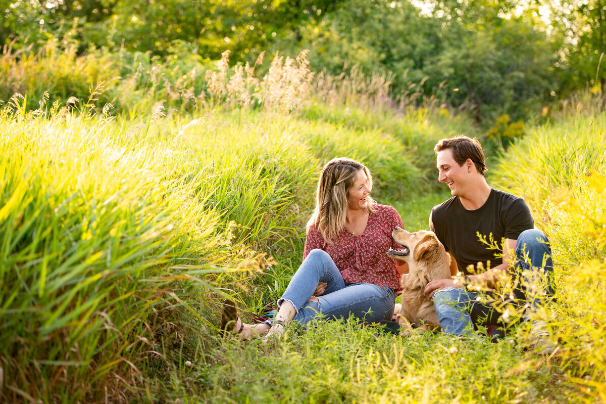 a couple sitting in a grassy field with their dog during family photography in Ottawa