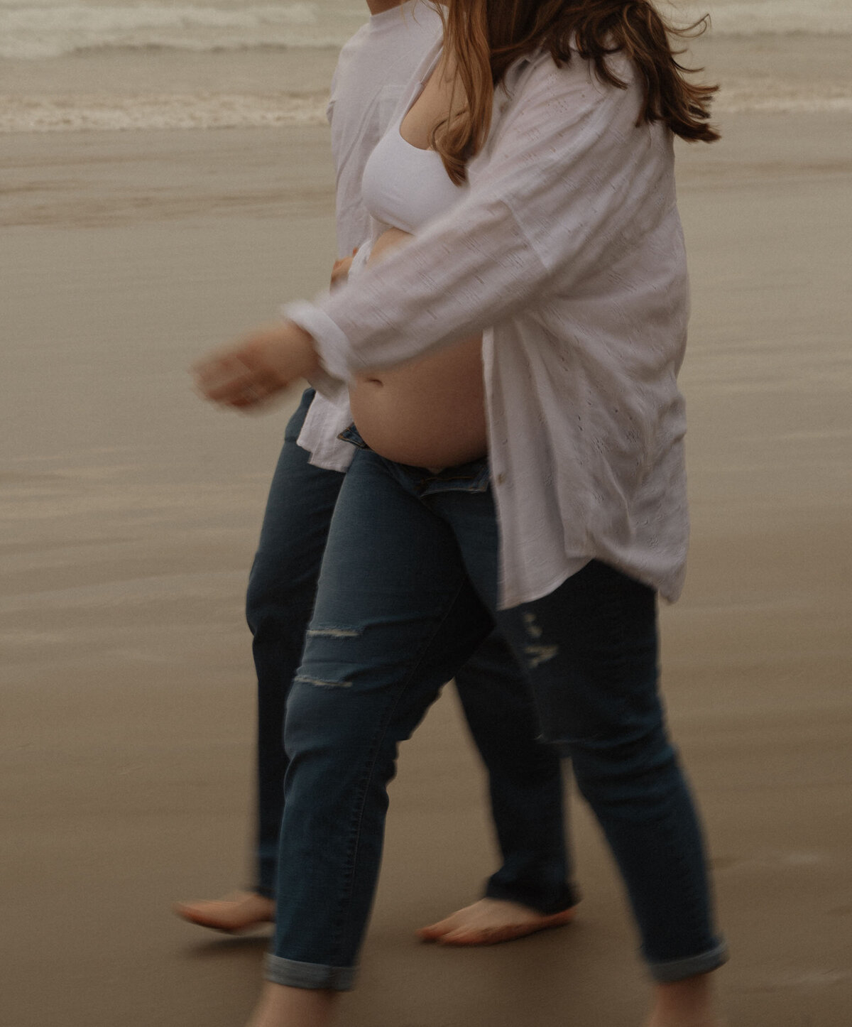 romantic maternity photo of couple walking hand in hand along the Oregon coast at sunset