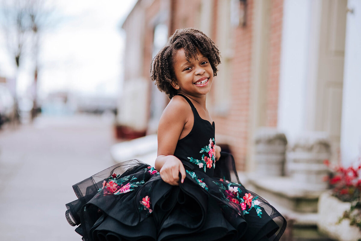 African American girl with curly brown hair smiling and holding a black floral dress on a city street in Fells Point Baltimore Maryland