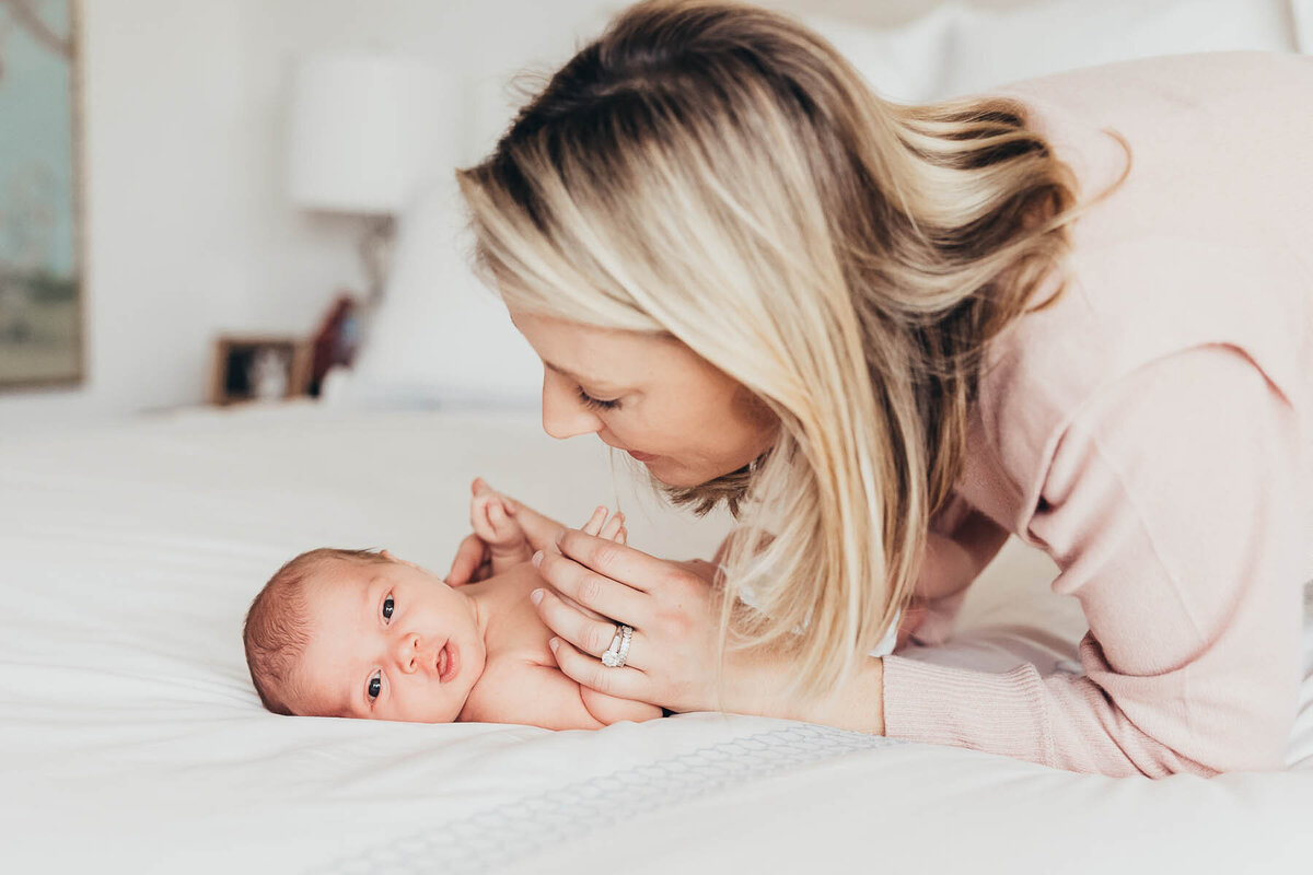 a mother leans over looking at her newborn baby in their del mar during their lifestyle newborn photography session with christine dammann in san diego