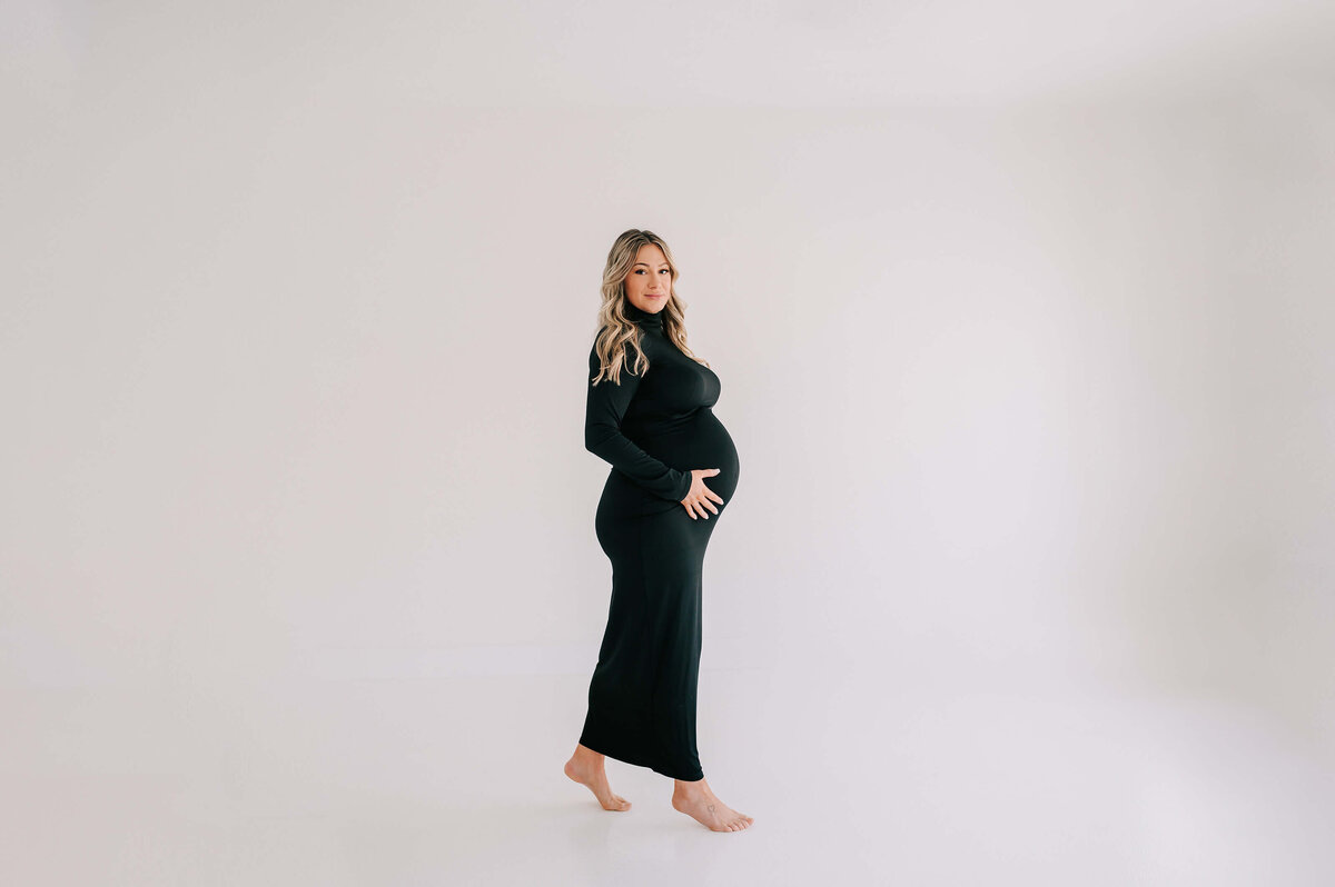 pregnant mom in black dress walking in studio during Branson MO maternity photography session