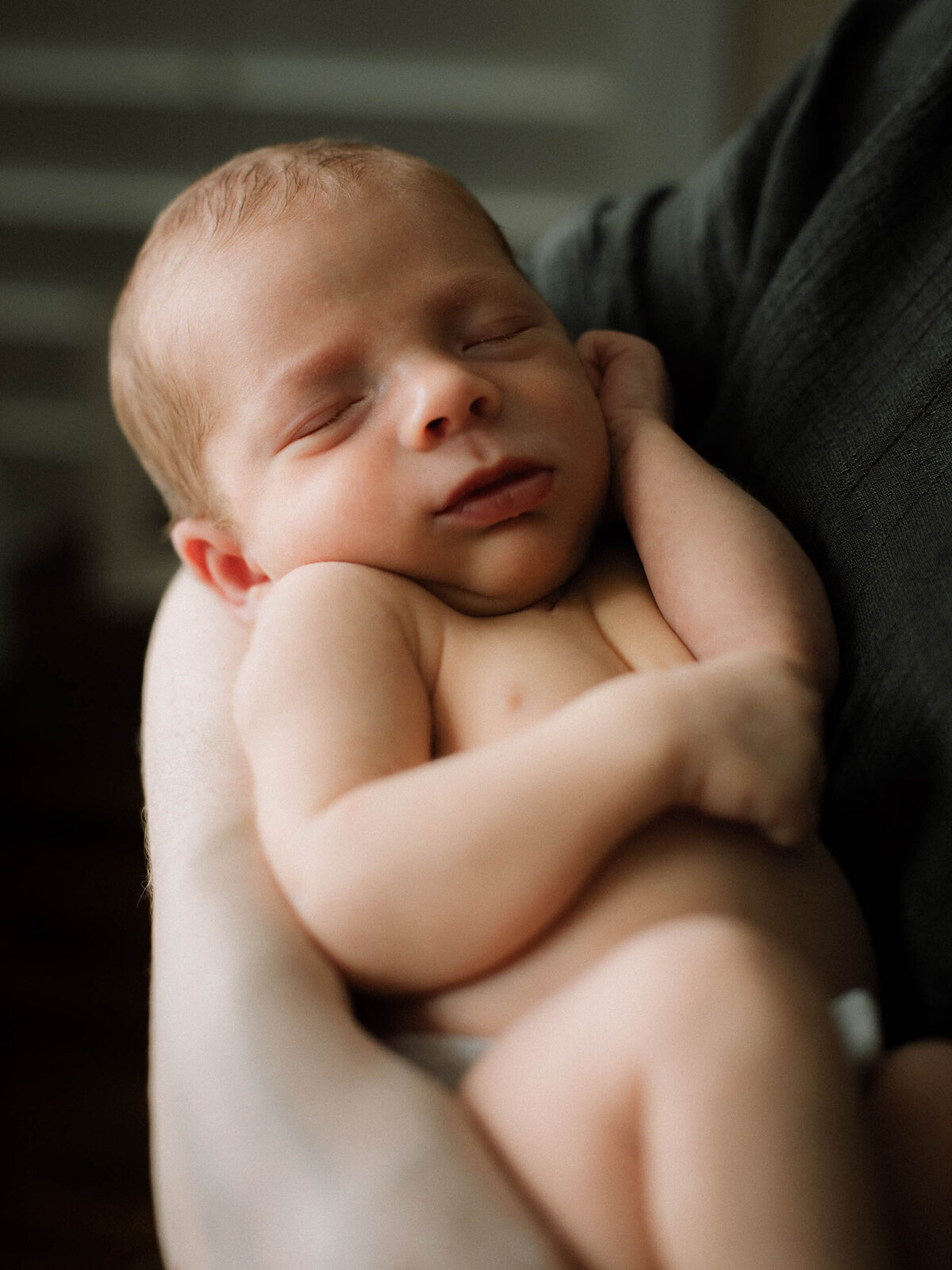 Baby portrait with hand resting on face, captured in natural light.
