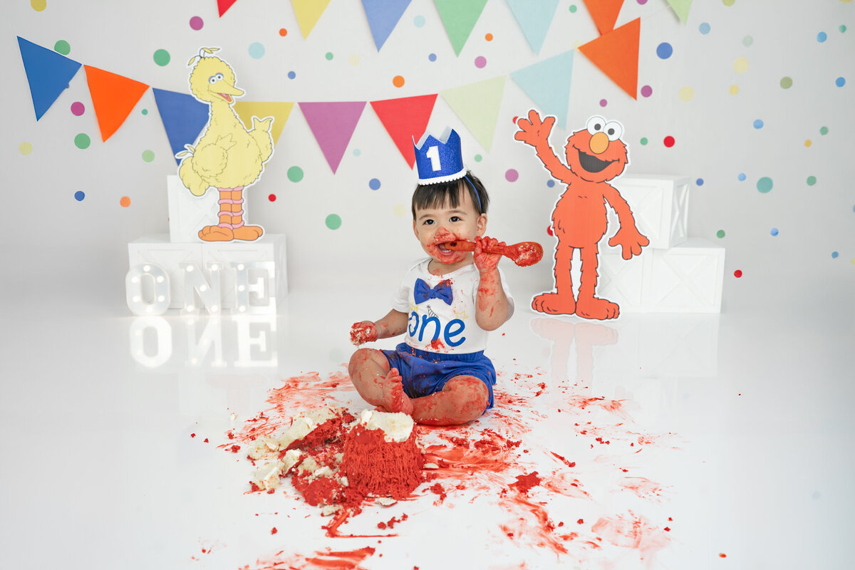 Boy in birthday outfit eating an Elmo cake during themed cake smash session— captured by Alliston and Barrie cake smash photographer.