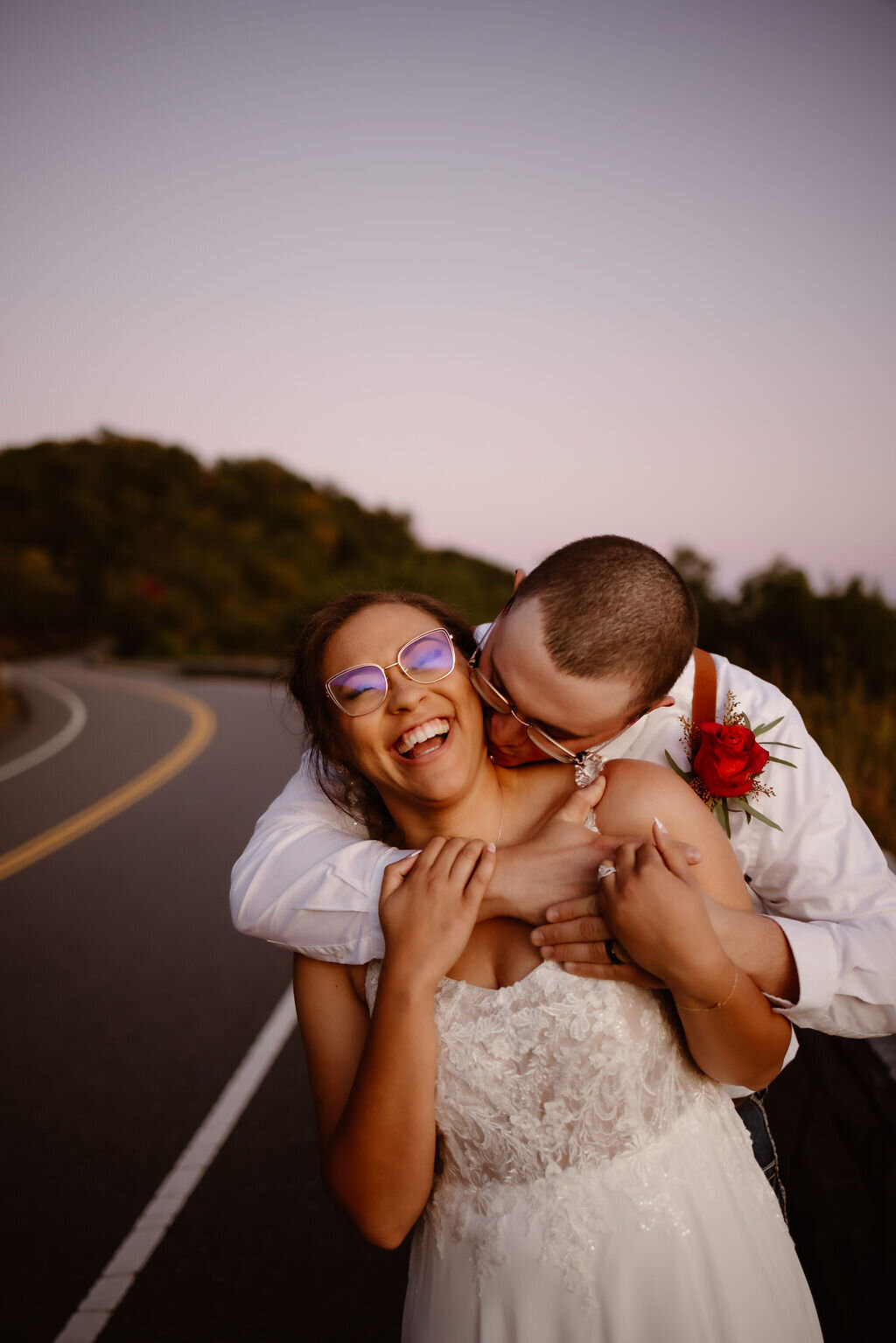 candid wedding photo of groom holding his bride around the shoulders and kissing her neck as she laughs captured by Gatlinburg photographers  