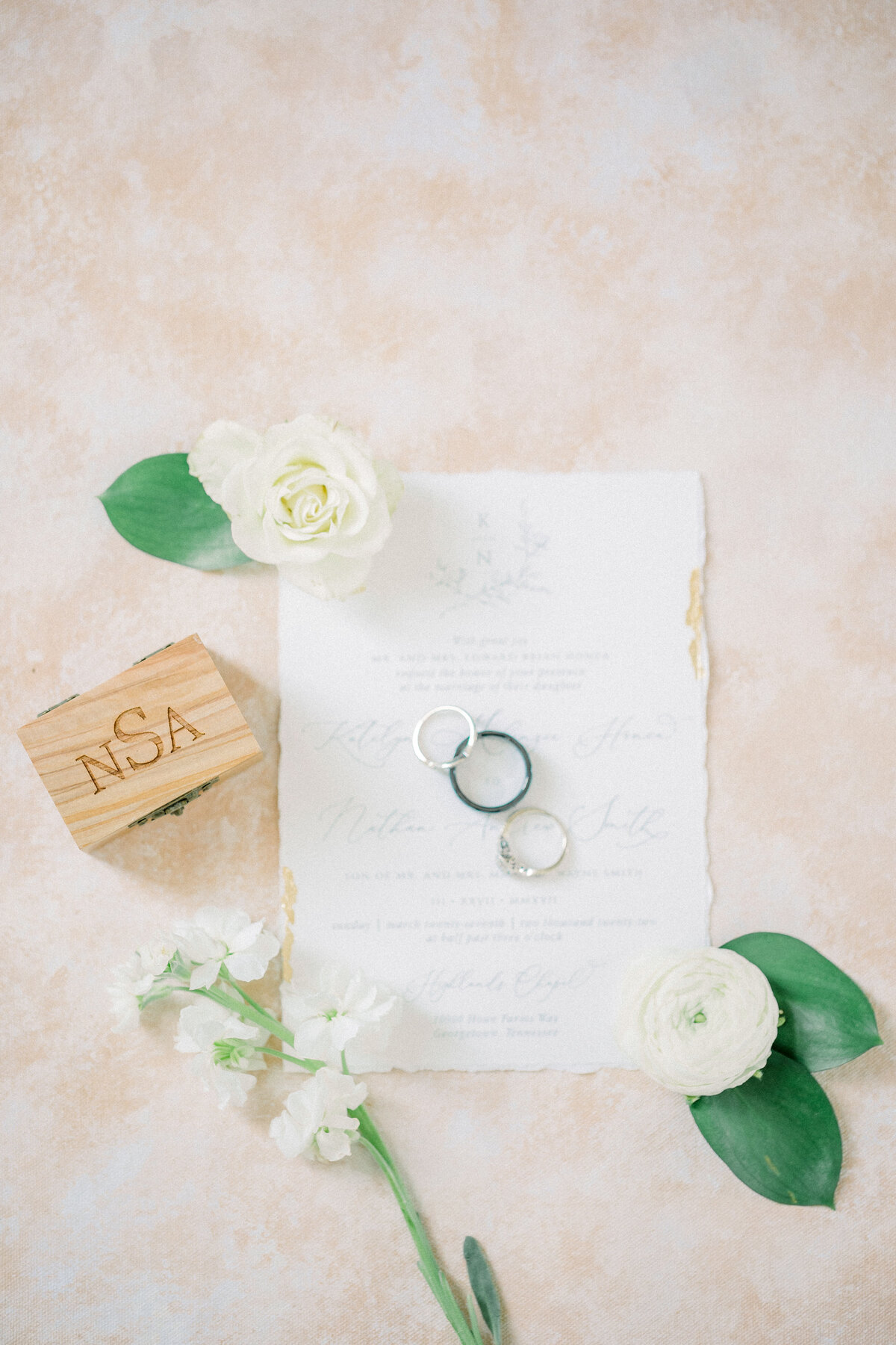 Bride and Groom rings on their invitation with white florals and greenery and their ring box