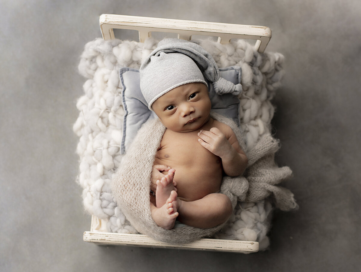 newborn baby boy wrapped in grey with grey sleepy cap looks curiously into the camera