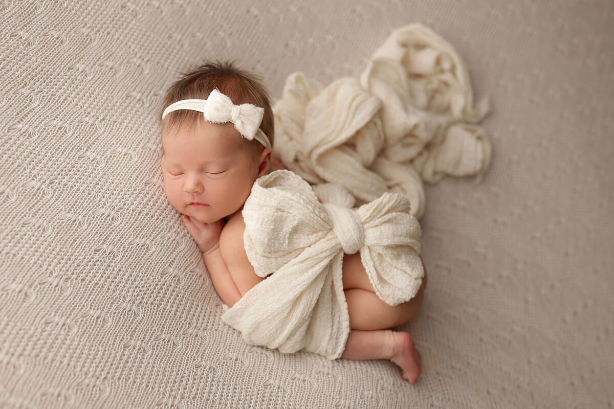 newborn baby girl sleeping on a white blanket with a big bow on top of her