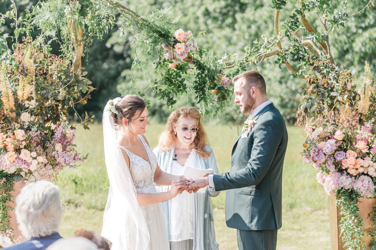 A bride and groom exchange rings in front of a glorious flower arch