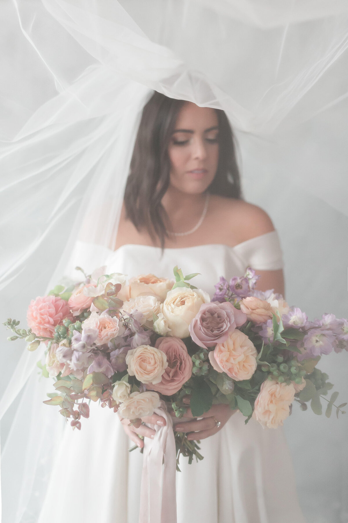 Bride holds lush water color bouquet as veil flies above