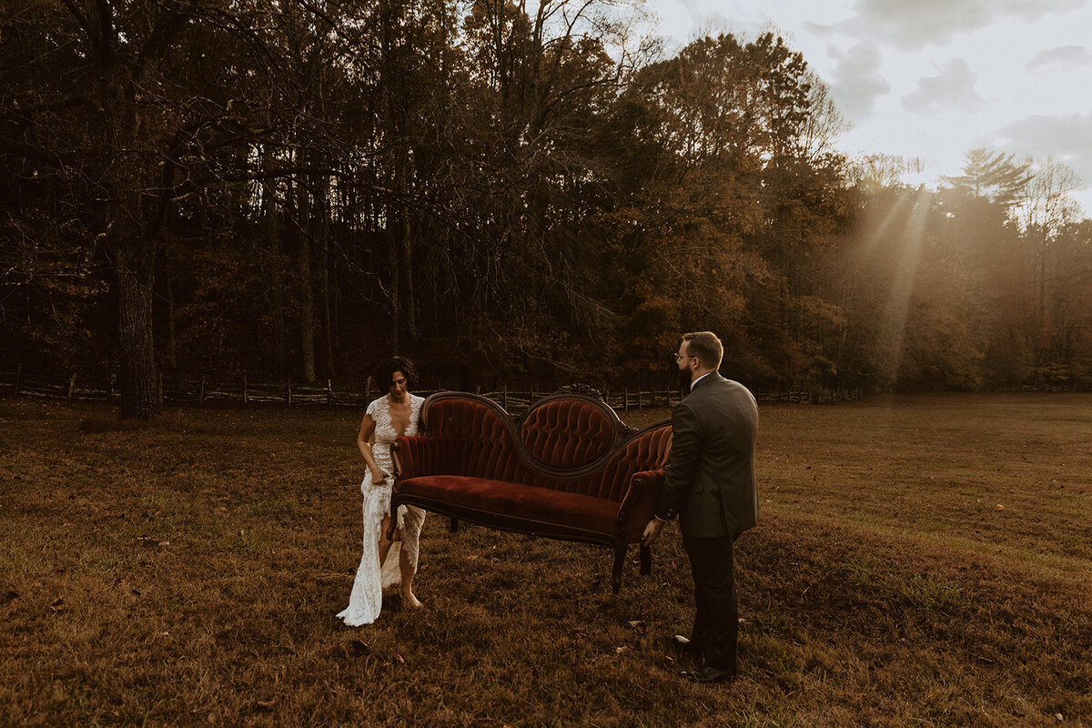 bride and groom carry red vintage couch through a field at neverland farms 