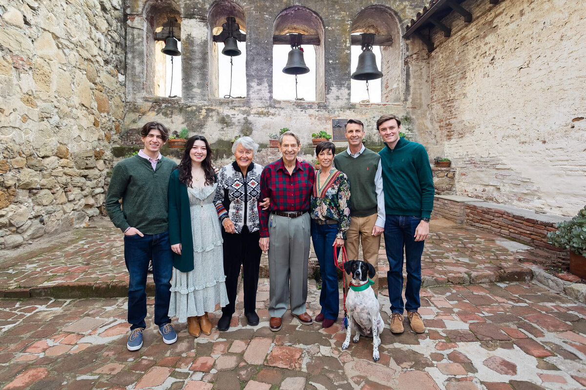 A family of five and two grandparents standing in a brick courtyard wearing shades of green and red.