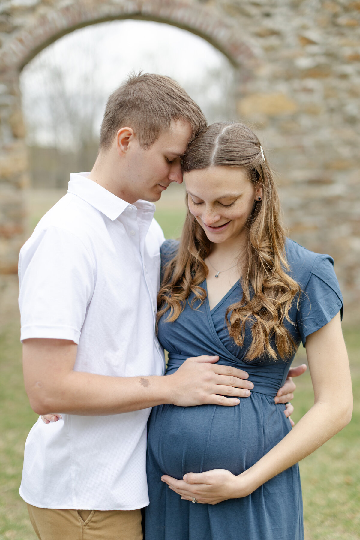 Soon to be parents snuggle close, each having a hand on the baby bump