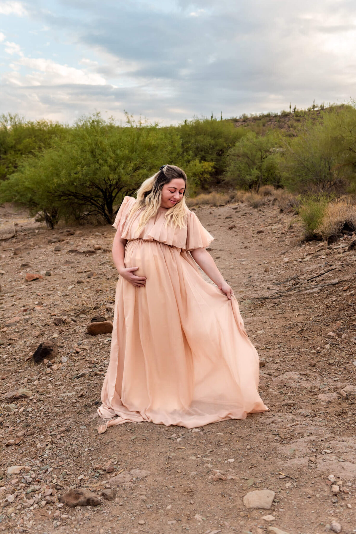 Expecting mom playing with train in gorgeous blush color gown. Captured by Cactus & Pine Photography