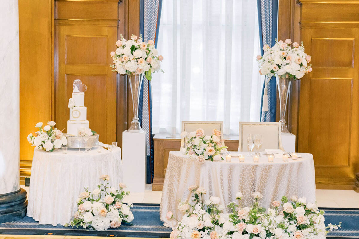 Sweetheart table with floral arrangements and cake nearby