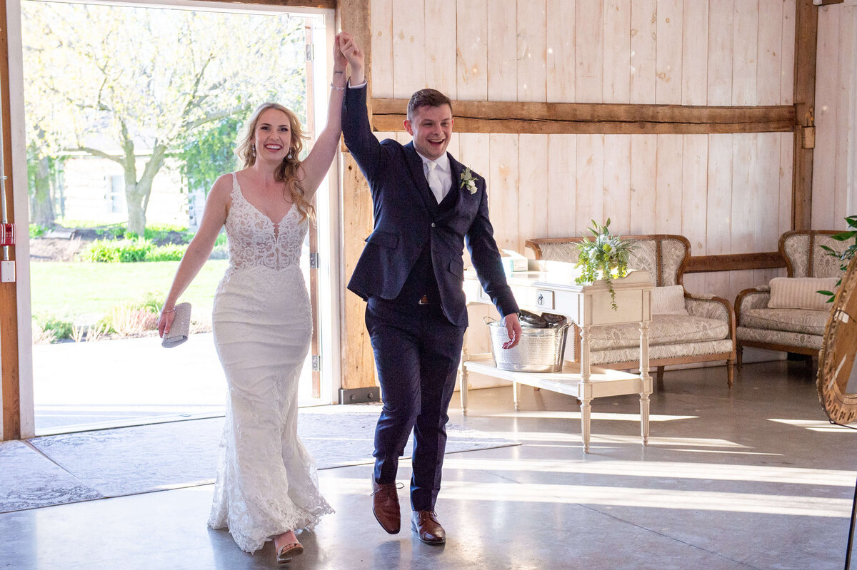 a bride and groom make their grand entrance to their reception at Stonefields Estate waving their arms in the air