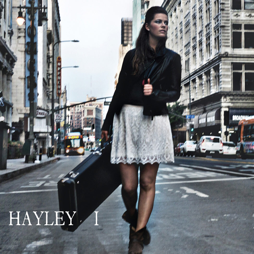 Album Cover Los Angeles Title I Artist Hayley walking down middle of city street guitar case in hand clutching jacket