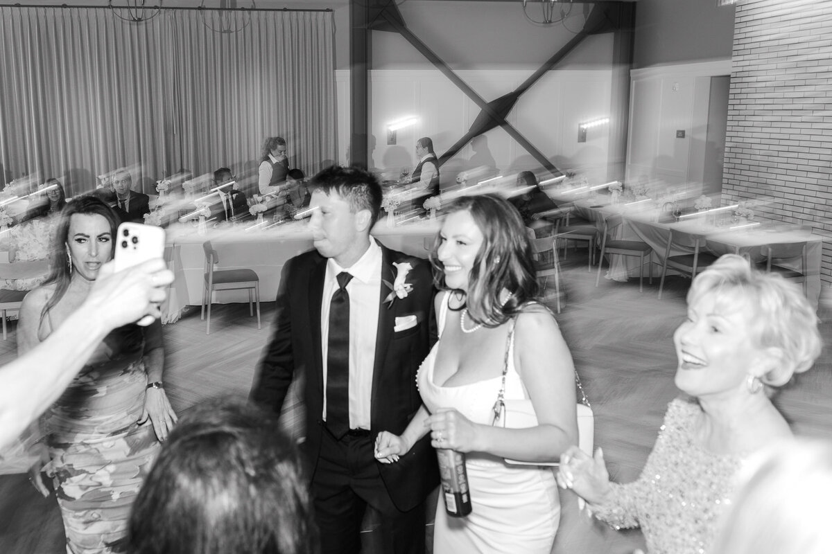 The bride and groom dance hand in hand with guests at their lively Lido House wedding reception in Newport Beach