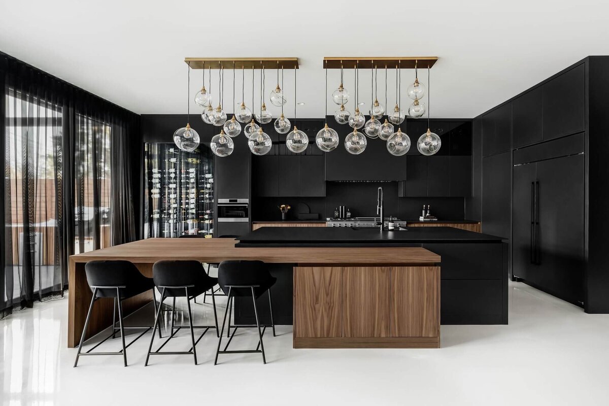 A bold dramatic kitchen with black dekton and walnut features and oversized pendant glass lighting. 