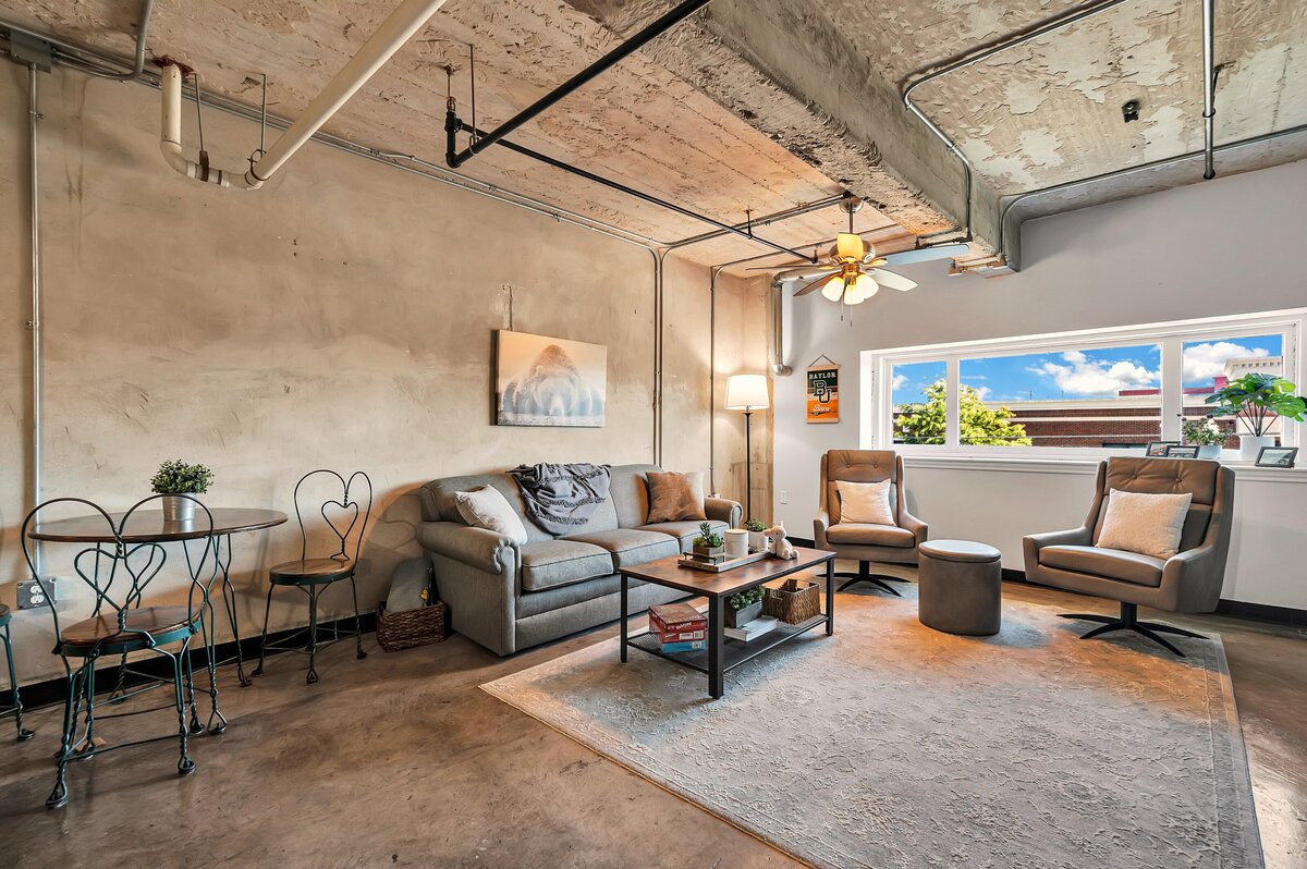 Living room with plenty of seating and incredible view in this one-bedroom, one-bathroom industrial vacation rental condo with free Wifi, onsite laundry, and space for four in the historic Behrens building of downtown Waco, TX.