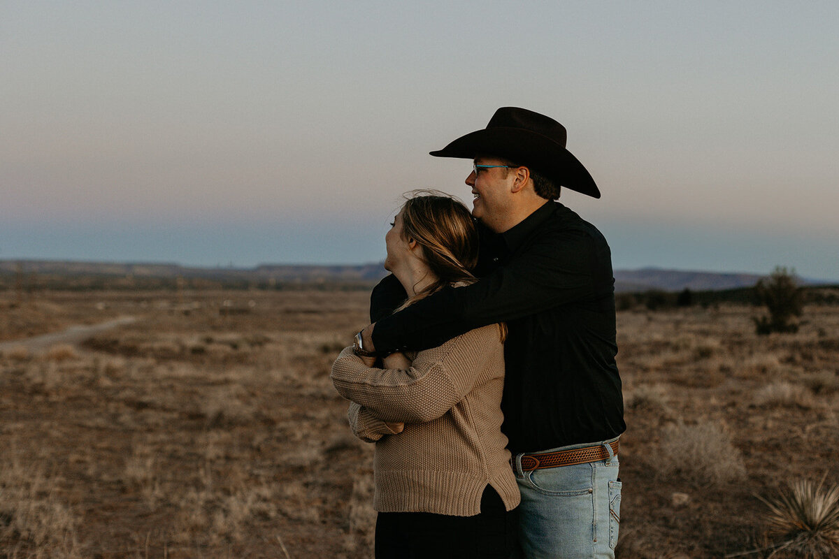 engaged couple holding each other looking off into the desert