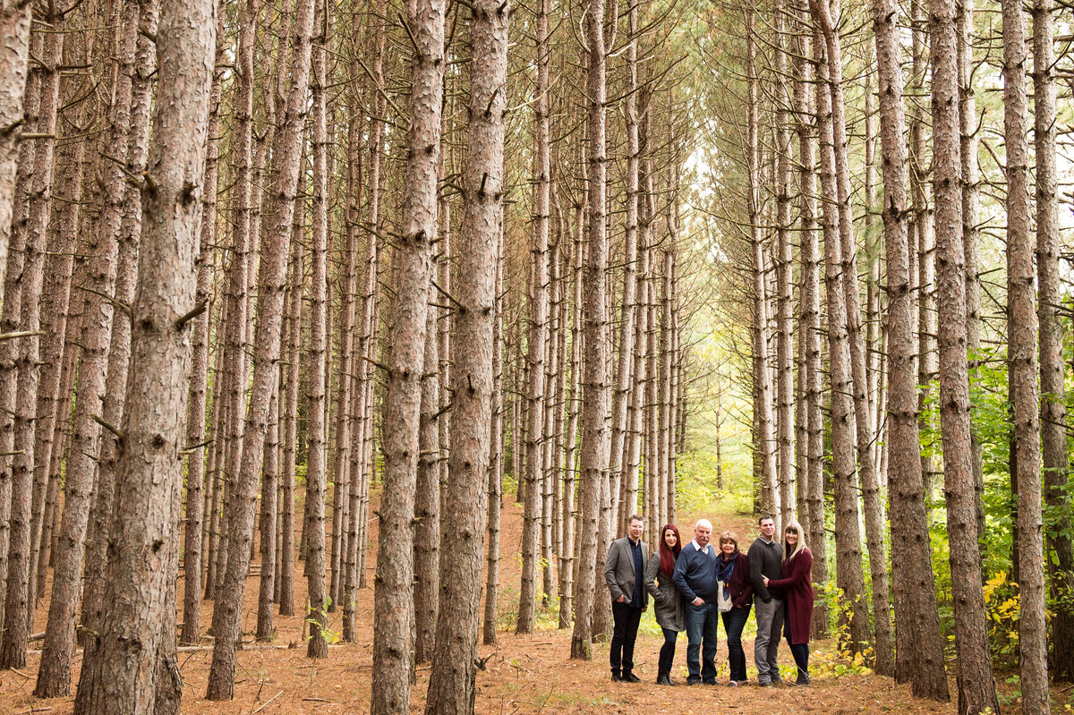 mom and dad with three adult children and their partners in a field of pine trees for their family photo