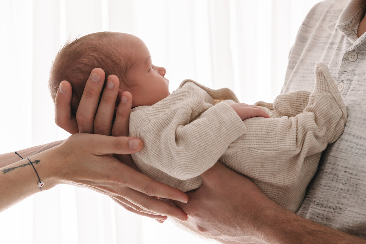pasgeboren baby gedragen door de handen van mama en papa in een neutrale setting