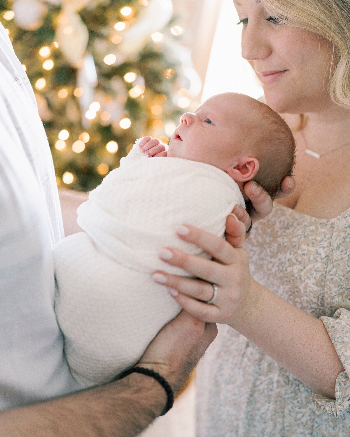 mom-and-dad-holding-newborn-in-front-of-christmas-trees