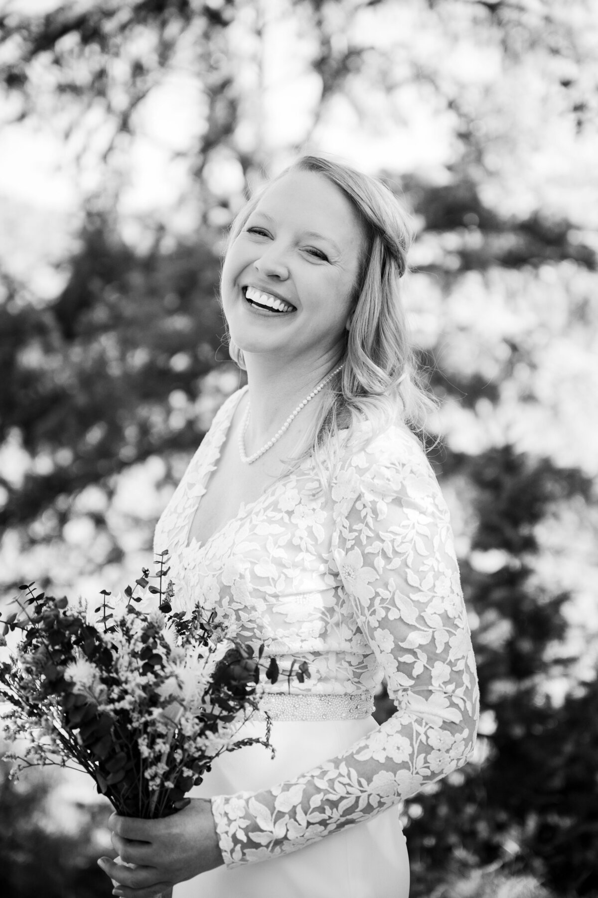 A bride in a long sleeve wedding dress throws her head back candidly and laughs.