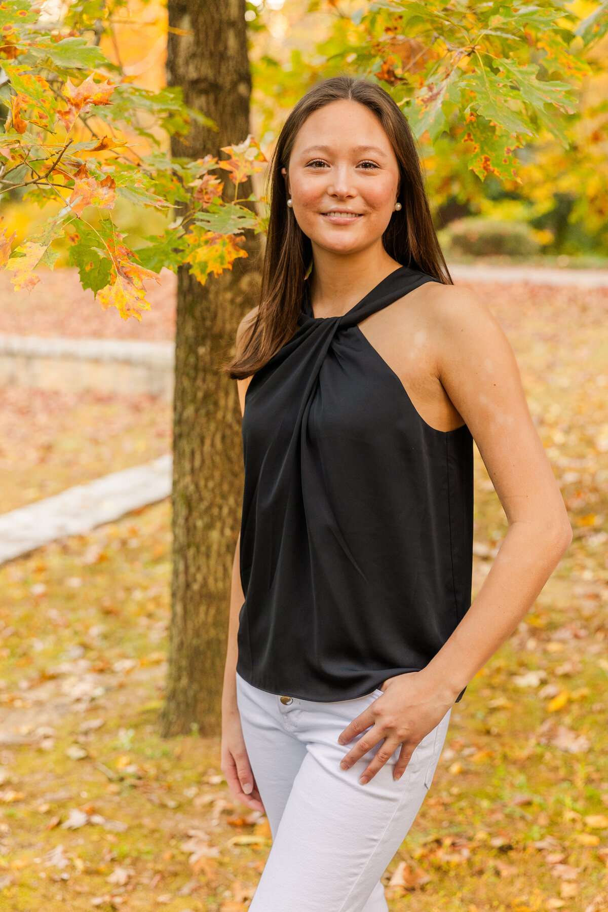 senior girl standing ankles crossed and in jeans' pocket smiling at the camera in an Atlanta park during portraits photo session