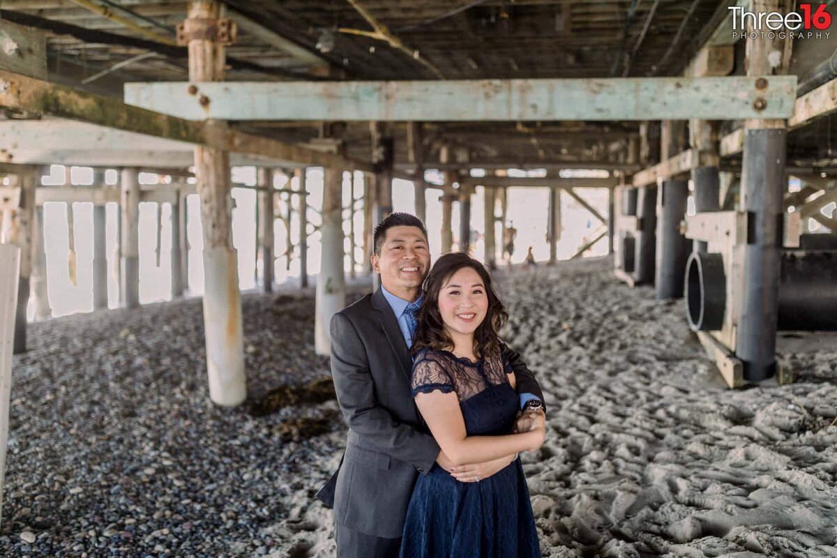 Engaged couple pose together in the sand under the San Clemente Pier