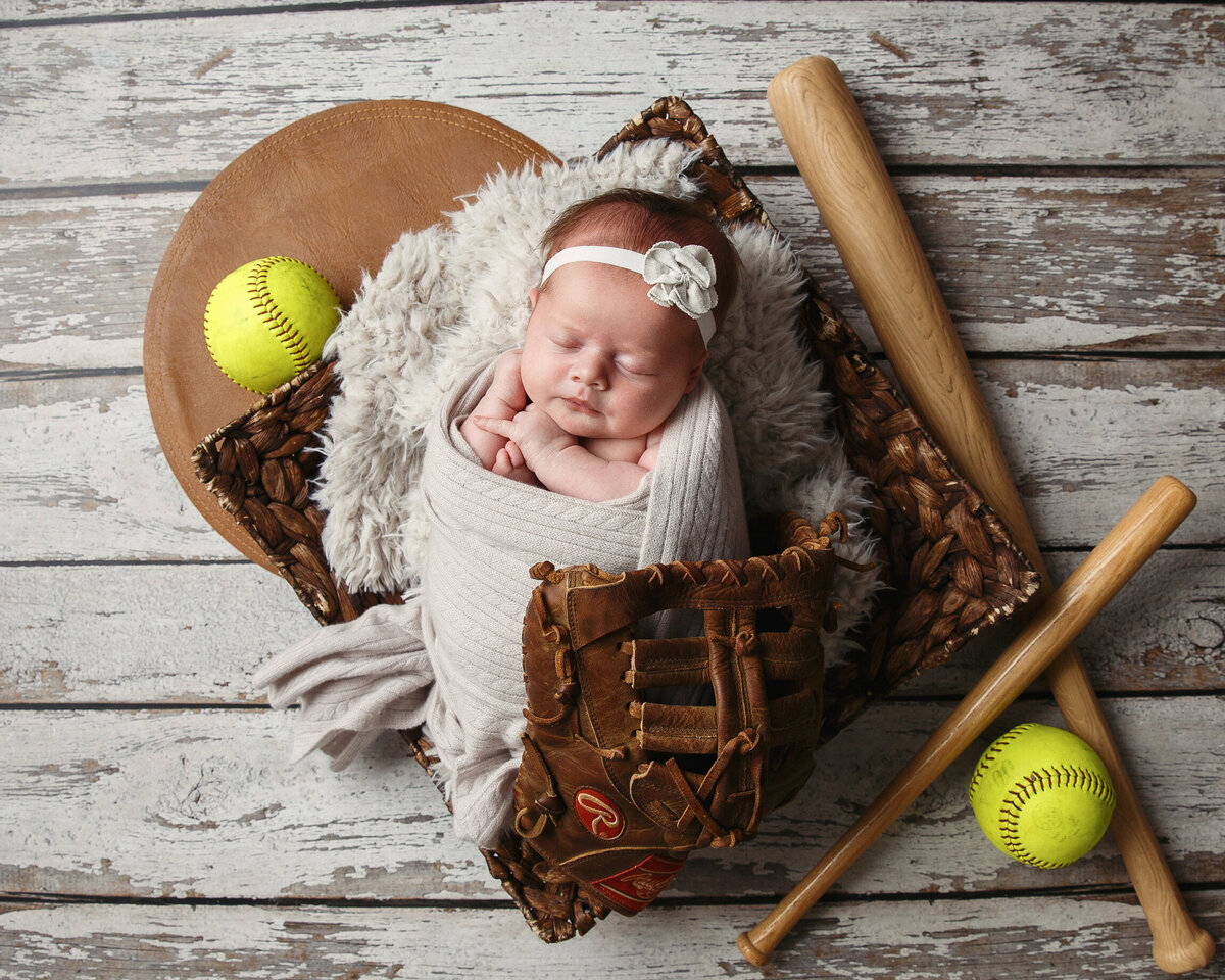 Newborn portrait of a baby with a baseball bat and softballs and glove