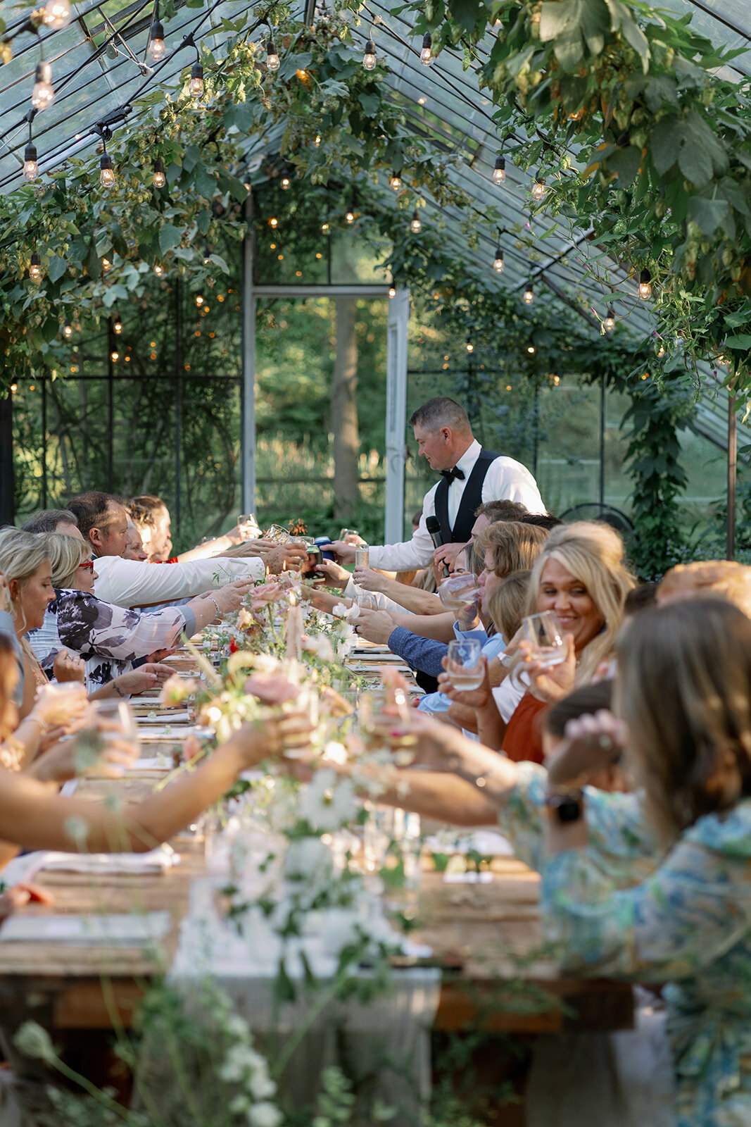 Guests raising glasses during dinner at the greenhouse reception at Glasshouse Community in Ottawa County, Michigan.