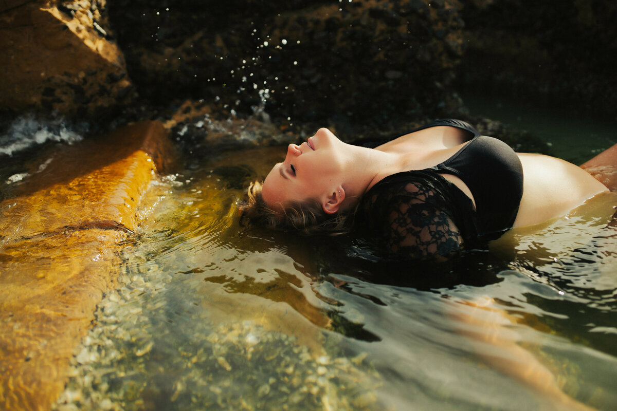 moody portraits of a  pregannt women laying in the water surrounded by ricks