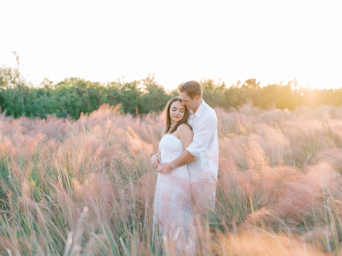 COuple embracing in a field of blooming pink grass at Cypress Point Park Engagement Session