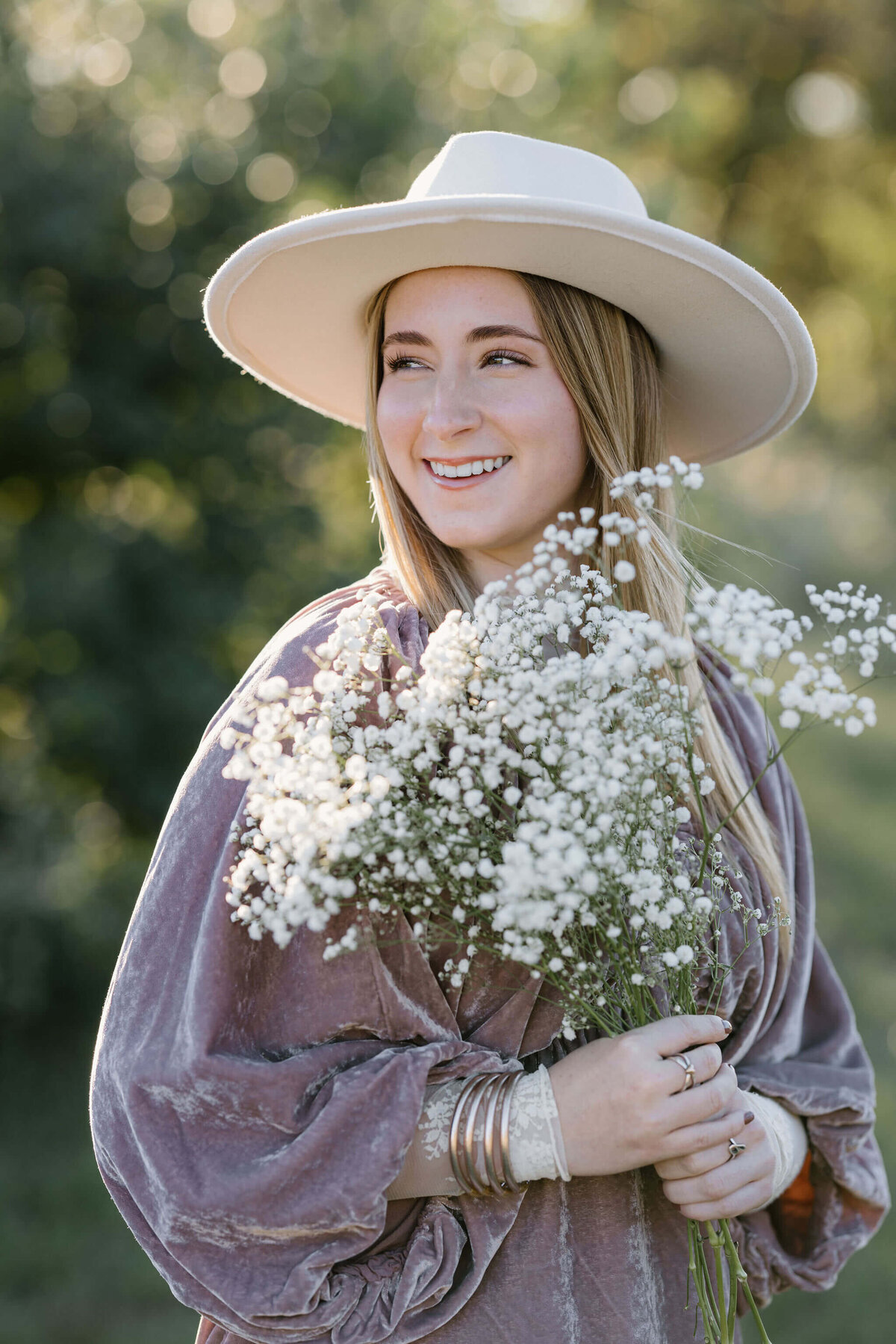 Marshall high school senior girl in pink velvet dress and white hat holding baby's breath flowers and laughing over shoulder