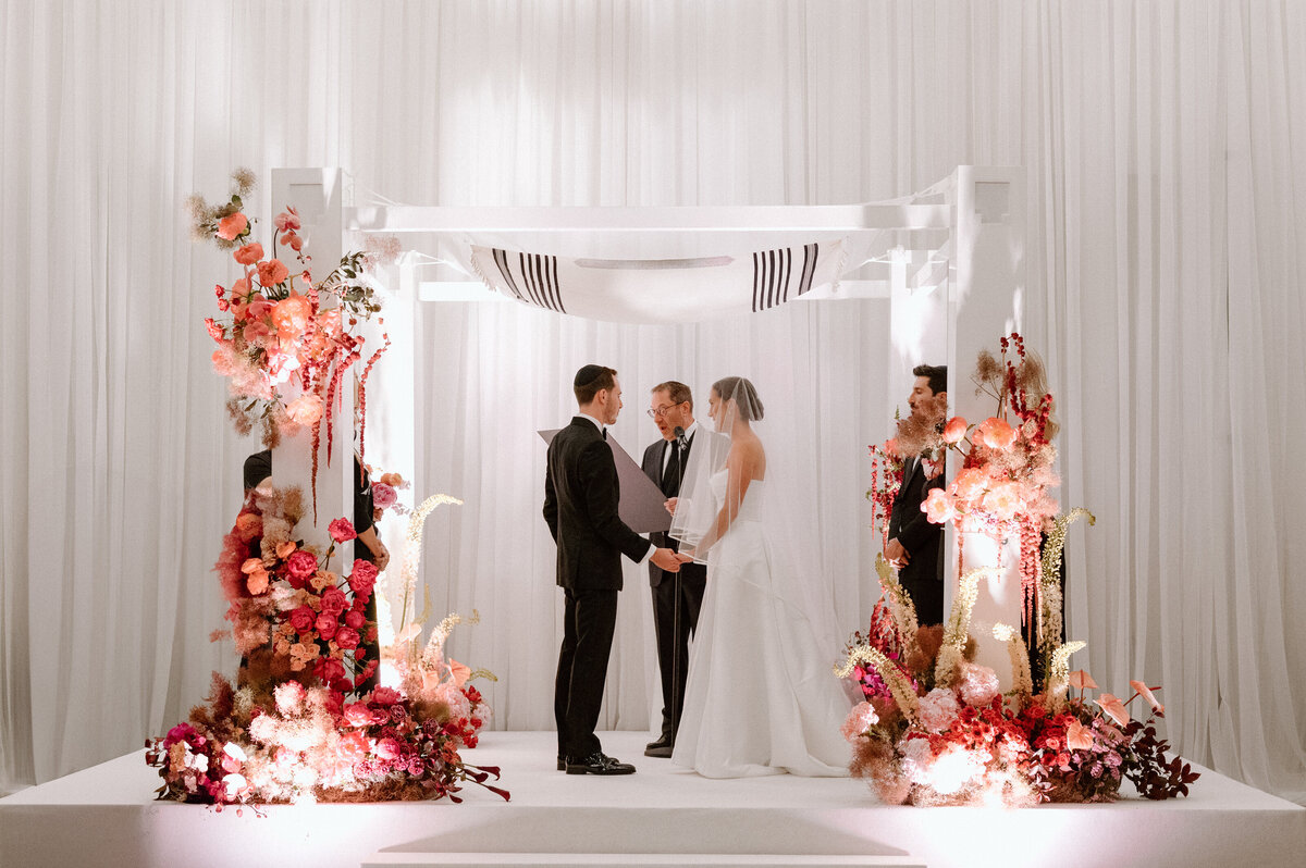 Bride and groom exchanging vows under a floral chuppah at an elegant Toronto wedding venue.