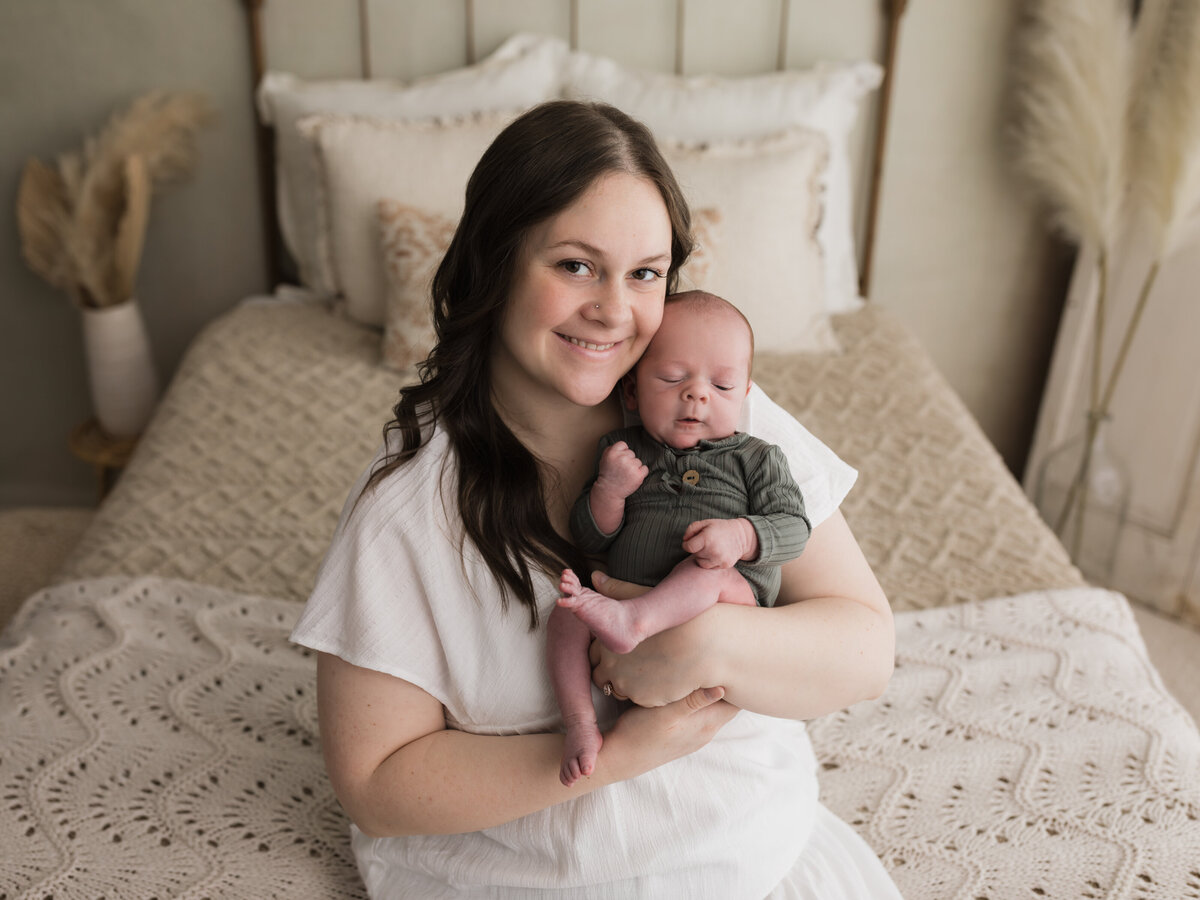 mom in white dress holding newborn baby boy in green onesie for studio portraits cleveland newborn photographer
