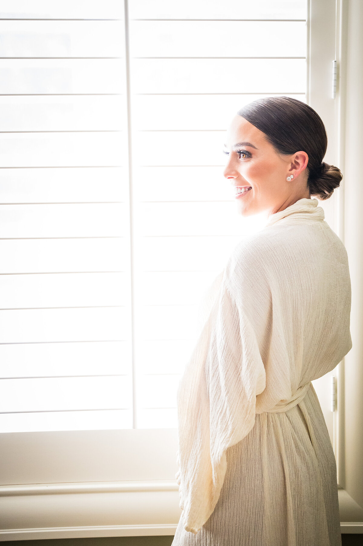 A candid shot of a bride in her getting ready robe smiling at something off camera.