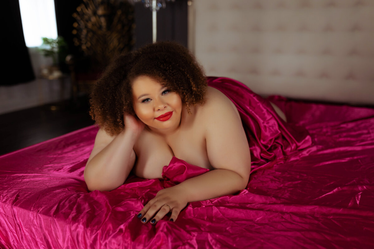 black woman nude during boudoir session wearing just pink sheets on bed