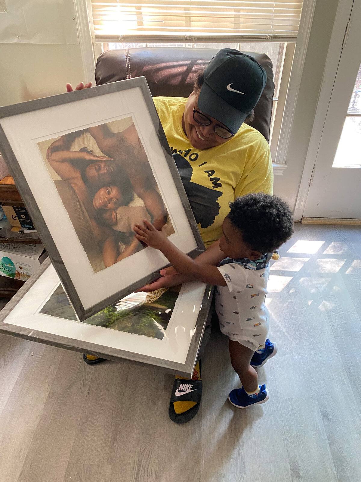 Charlotte mom celebrates baby's arrival, opening framed newborn photos with her excited toddler, who proudly holds his baby picture.