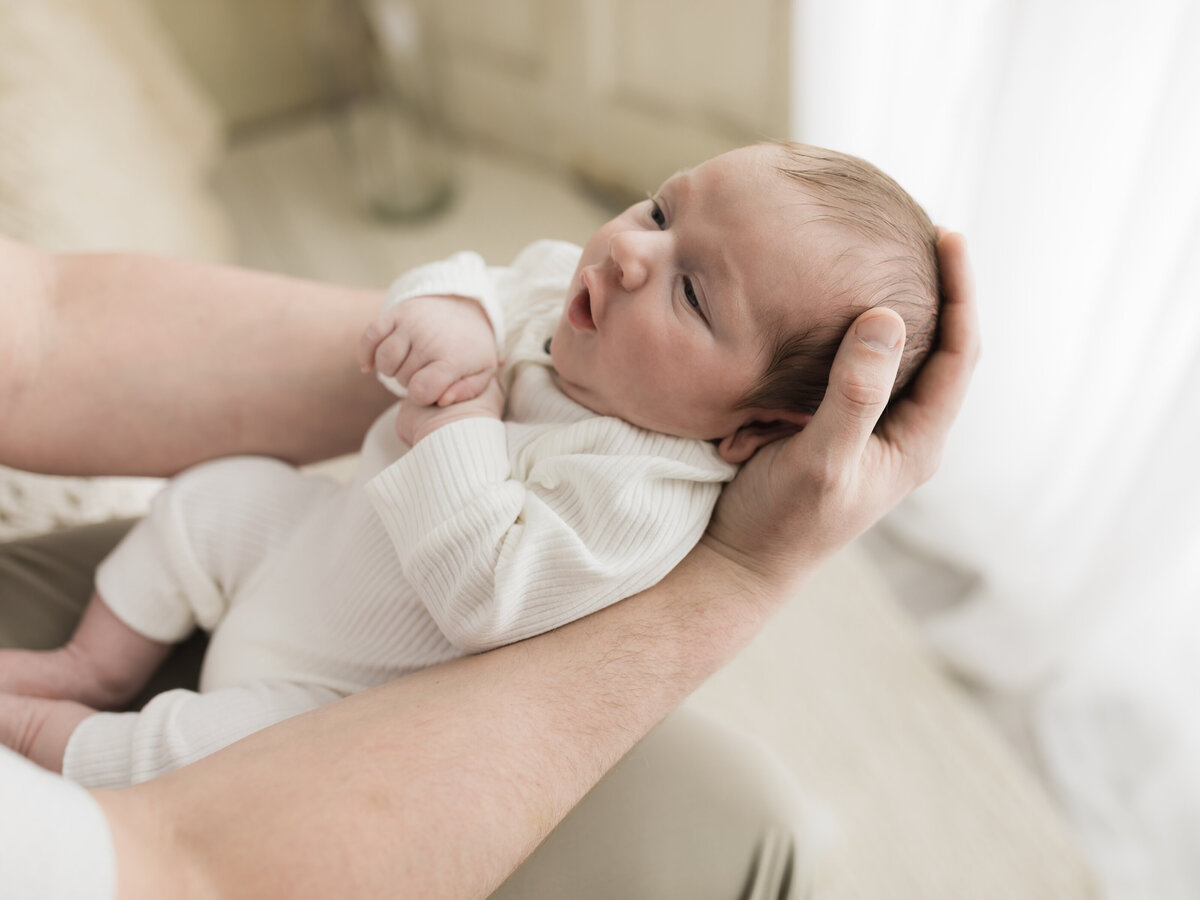 dad holding newborn baby boy in white onesie for studio photoshoot 